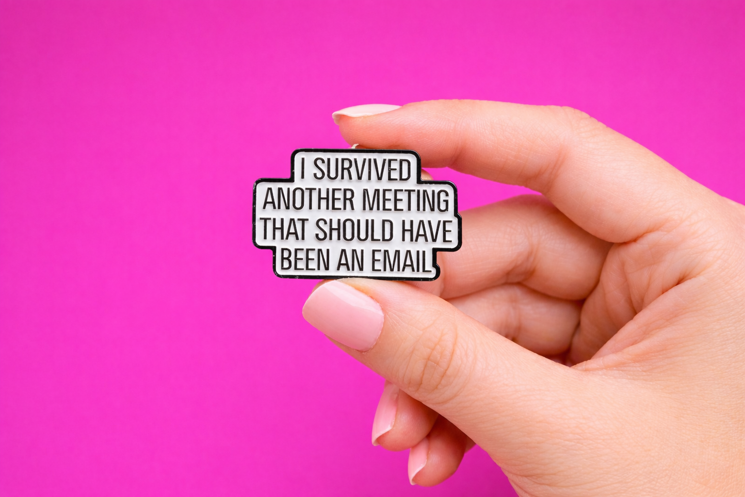 Hand holding a pin with text 'I survived another meeting that should have been an email' against a pink background